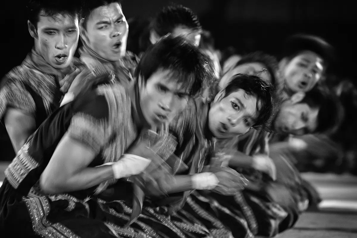 A line of Saman dancers in dark embroidered costumes, caught in motion in black and white as they sway together